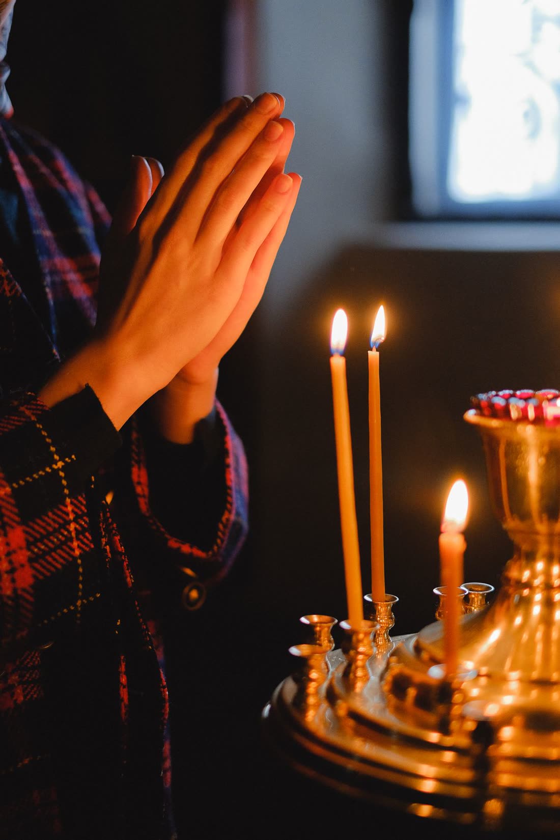 Mãos em oração diante de velas acesas